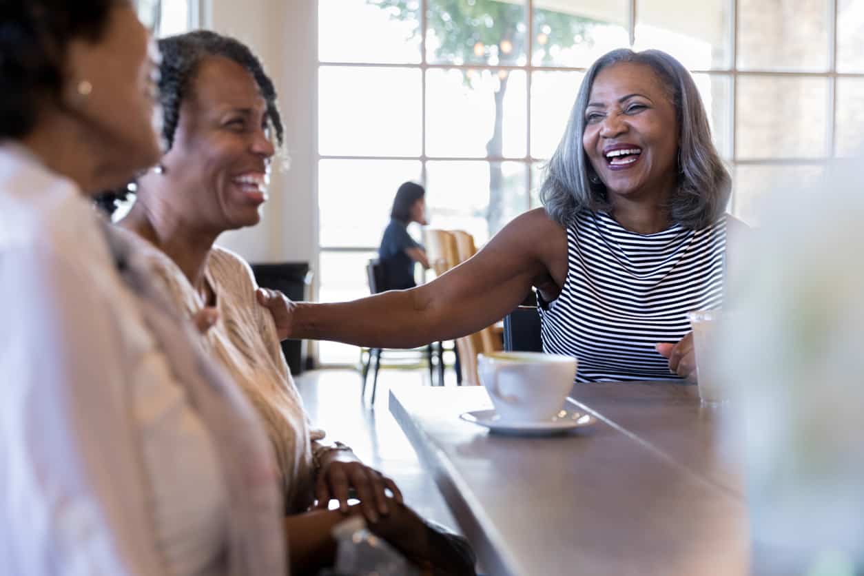 Mature adult female friends laugh when they meet at cafe